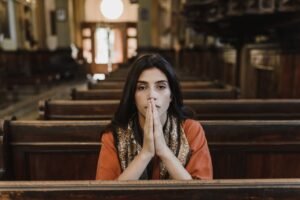 A woman in a church pew with folded hands, symbolizing faith, prayer, and contemplation.